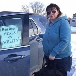 A volunteer driver beside her car with a Red Deer Meals on Wheels sign